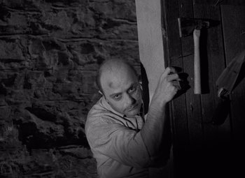 Movie still from “Night of the Living Dead” (1968), directed by George A. Romero – A man holding onto a door handle in a dark room; Medium shot, High angle