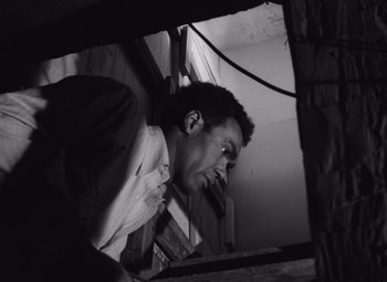Movie still from “Night of the Living Dead” (1968), directed by George A. Romero – A black and white photo of a man smoking a cigarette; Close Up shot, Low angle