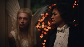 Movie still from “Euphoria” (2019), created by Sam Levinson – Two women in formal wear standing next to each other in front of lights; Medium shot, Over the shoulder angle