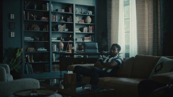 Movie still from “Atlanta” (2016), created by Donald Glover – A man sitting on top of a brown couch in a living room; Wide shot, Low angle