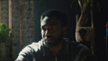 Movie still from “Atlanta” (2016), created by Donald Glover – A man sitting in front of a brick wall looking off to his right; Close Up shot, Over the shoulder angle