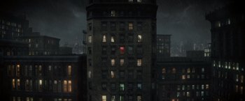Movie still from “Nightbooks” (2021), directed by David Yarovesky – A tall building with many windows in the dark; Extreme Wide shot, Overhead angle