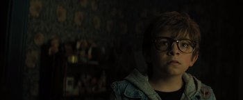 Movie still from “Nightbooks” (2021), directed by David Yarovesky – A person wearing glasses and a jean jacket in a room; Close Up shot, Low angle