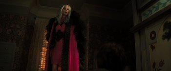 Movie still from “Nightbooks” (2021), directed by David Yarovesky – A woman in a pink dress and a black boa; Medium shot, Over the shoulder angle