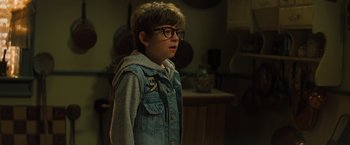 Movie still from “Nightbooks” (2021), directed by David Yarovesky – A young boy wearing glasses and a jean jacket; Close Up shot, Over the shoulder angle