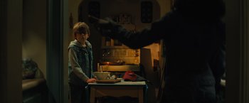 Movie still from “Nightbooks” (2021), directed by David Yarovesky – Two people in a kitchen one is holding a bowl and the other is holding a knife; Medium shot, Over the shoulder angle