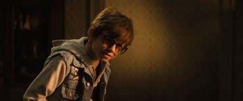 Movie still from “Nightbooks” (2021), directed by David Yarovesky – A young boy wearing glasses and a jean jacket; Close Up shot, Over the shoulder angle
