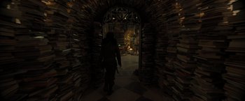 Movie still from “Nightbooks” (2021), directed by David Yarovesky – A person walking through a tunnel of stacks of books; Wide shot, Low angle