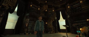 Movie still from “Nightbooks” (2021), directed by David Yarovesky – A young boy standing in front of a bookcase in a library; Wide shot, Low angle