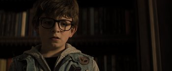 Movie still from “Nightbooks” (2021), directed by David Yarovesky – A young boy wearing glasses and a jean jacket; Close Up shot, Over the shoulder angle