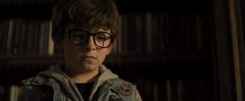 Movie still from “Nightbooks” (2021), directed by David Yarovesky – A young boy wearing glasses and a jean jacket; Close Up shot, Over the shoulder angle