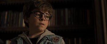Movie still from “Nightbooks” (2021), directed by David Yarovesky – A young boy wearing glasses and a jean jacket; Close Up shot, High angle