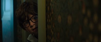 Movie still from “Nightbooks” (2021), directed by David Yarovesky – A young boy wearing glasses leaning against a wall; Close Up shot, Over the shoulder angle