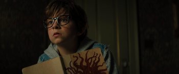 Movie still from “Nightbooks” (2021), directed by David Yarovesky – A boy with glasses holding up an octopus sign; Close Up shot, High angle