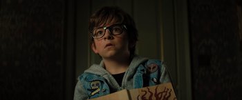 Movie still from “Nightbooks” (2021), directed by David Yarovesky – A young boy wearing glasses and holding a book; Close Up shot, High angle