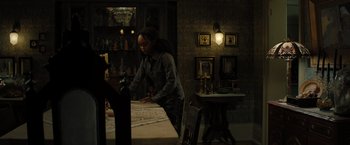 Movie still from “Nightbooks” (2021), directed by David Yarovesky – A woman standing at a table in a dark room; Medium shot, High angle