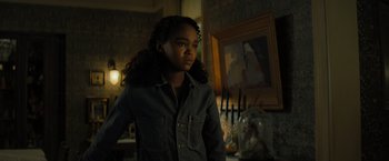 Movie still from “Nightbooks” (2021), directed by David Yarovesky – A young girl standing in front of a painting in a dark room; Medium shot, Low angle