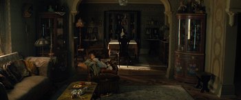 Movie still from “Nightbooks” (2021), directed by David Yarovesky – A woman sitting in a chair in a living room; Wide shot, High angle