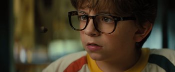 Movie still from “Nightbooks” (2021), directed by David Yarovesky – A young boy wearing glasses looking at the camera; Close Up shot, High angle