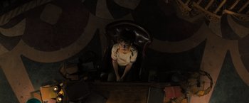 Movie still from “Nightbooks” (2021), directed by David Yarovesky – A young boy sitting in a chair in a room; Medium shot, Overhead angle