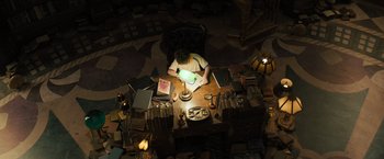 Movie still from “Nightbooks” (2021), directed by David Yarovesky – An overhead view of a person sitting at a table with a lamp; Wide shot, High angle