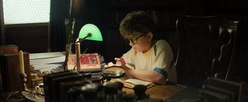 Movie still from “Nightbooks” (2021), directed by David Yarovesky – A young boy sitting at a table with a book; Medium shot, High angle
