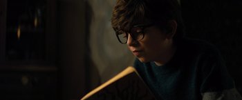 Movie still from “Nightbooks” (2021), directed by David Yarovesky – A young man wearing glasses reading a book in a dark room; Close Up shot, Over the shoulder angle