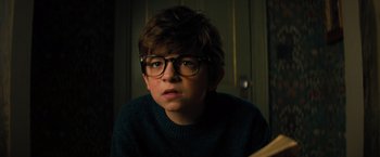 Movie still from “Nightbooks” (2021), directed by David Yarovesky – A young boy wearing glasses and a green sweater; Close Up shot, High angle
