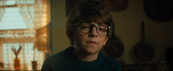 Movie still from “Nightbooks” (2021), directed by David Yarovesky – A young boy wearing glasses and a green sweater; Close Up shot, Low angle