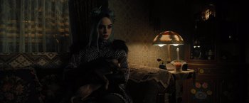 Movie still from “Nightbooks” (2021), directed by David Yarovesky – A woman sitting on a couch holding a cat in her arms; Medium shot, High angle