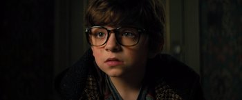 Movie still from “Nightbooks” (2021), directed by David Yarovesky – A young boy wearing glasses and a sweater; Close Up shot, High angle