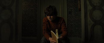 Movie still from “Nightbooks” (2021), directed by David Yarovesky – A person sitting on the ground reading a book; Medium shot, High angle