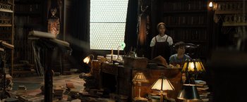 Movie still from “Nightbooks” (2021), directed by David Yarovesky – A man sitting at a desk in a room with many lamps; Wide shot, High angle