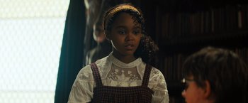 Movie still from “Nightbooks” (2021), directed by David Yarovesky – A young girl wearing a white shirt and a plaid dress; Close Up shot, Over the shoulder angle