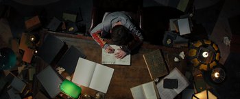 Movie still from “Nightbooks” (2021), directed by David Yarovesky – A person sitting at a table writing on a book; Medium shot, Overhead angle