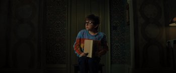 Movie still from “Nightbooks” (2021), directed by David Yarovesky – A person sitting in a room holding a book; Medium shot, High angle