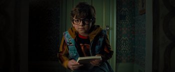 Movie still from “Nightbooks” (2021), directed by David Yarovesky – A young boy is holding a book in his hands; Medium shot, High angle