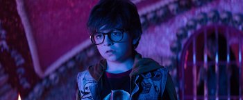 Movie still from “Nightbooks” (2021), directed by David Yarovesky – A young boy wearing glasses in a dark room; Close Up shot, Over the shoulder angle