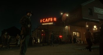 Movie still from “Nightmare Alley” (2021), directed by Guillermo del Toro – A man standing in front of a cafe at night; Wide shot, Low angle