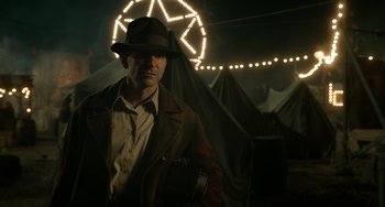 Movie still from “Nightmare Alley” (2021), directed by Guillermo del Toro – A man wearing a hat and a jacket in front of tents; Medium shot, Low angle