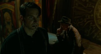Movie still from “Nightmare Alley” (2021), directed by Guillermo del Toro – A man smoking a cigarette while another man smokes a cigarette in the background; Close Up shot, Over the shoulder angle
