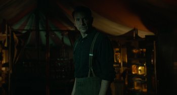 Movie still from “Nightmare Alley” (2021), directed by Guillermo del Toro – A man wearing suspenders standing in front of a tent; Medium shot, Low angle