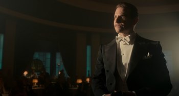 Movie still from “Nightmare Alley” (2021), directed by Guillermo del Toro – A man in a tuxedo standing in front of a table; Medium shot, Low angle