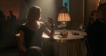 Movie still from “Nightmare Alley” (2021), directed by Guillermo del Toro – A woman sitting at a table smoking a cigarette; Medium shot, Low angle