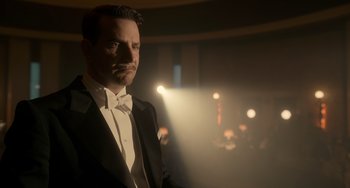 Movie still from “Nightmare Alley” (2021), directed by Guillermo del Toro – A man in a tuxedo standing in front of lights; Medium shot, Low angle