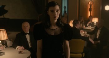 Movie still from “Nightmare Alley” (2021), directed by Guillermo del Toro – A woman in a black dress standing in front of a group of people; Medium shot, Over the shoulder angle