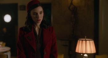 Movie still from “Nightmare Alley” (2021), directed by Guillermo del Toro – A woman in a red coat standing next to a lamp; Medium shot, Over the shoulder angle