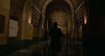 Movie still from “Nightmare Alley” (2021), directed by Guillermo del Toro – A man wearing a hat walking through a hallway; Extreme Wide shot, Low angle