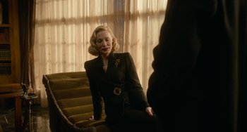 Movie still from “Nightmare Alley” (2021), directed by Guillermo del Toro – A woman in a black suit sitting on a chair; Medium shot, Low angle
