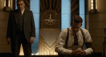 Movie still from “Nightmare Alley” (2021), directed by Guillermo del Toro – A man sitting in front of another man in front of a building; Medium shot, Low angle